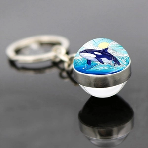 Close-up of glass ball keychain featuring an orca leaping over waves on a mirror base
