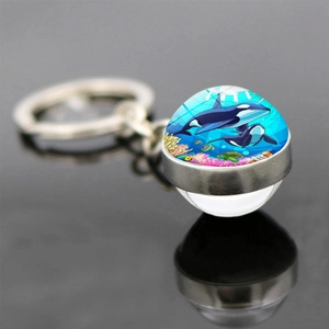 Close-up of double-sided glass ball keychain with ocean orca family and coral reef illustration