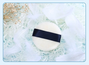 Detailed close-up of a round white plush makeup puff with a navy blue ribbon handle