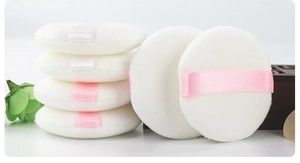 Detailed stack of round plush powder puffs with soft ribbon handles for makeup setting