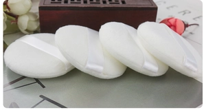 Detail of four white plush powder puffs with ribbon handles for smooth makeup application
