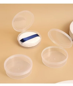 Close-up of a white plush powder puff with blue ribbon in a clear plastic storage case