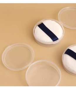 Detailed macro view of soft white velvet powder puff with dark blue ribbon in clear box
