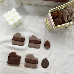Close-up of chocolate-themed makeup puffs in a mini shopping cart on a white fabric background