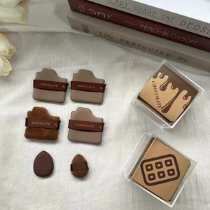 Chocolate-themed makeup puff set with sponges and clear storage boxes on white fabric