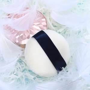 Round plush makeup powder puff with dark blue ribbon handle and rose gold lid