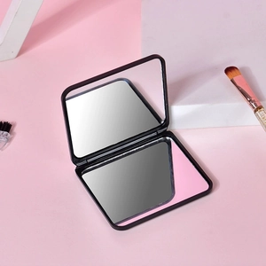 Miroir de maquillage noir carré pliable double face sur fond rose avec accessoires