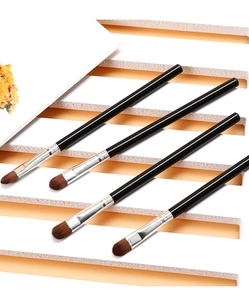 Nahaufnahme von vier Concealer-Pinseln mit schwarzen Griffen auf gestreiftem weißem Podest