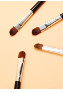 Makro-Detail von vier flachen Concealer-Pinseln mit schwarzen Griffen und Synthetikborsten