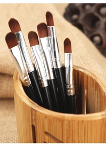 Makroaufnahme von 7 synthetischen Make-up-Pinseln in einem gestreiften Bambushalter