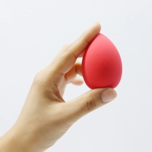 Macro detail of red teardrop makeup sponge showing fine texture and ergonomic hand grip