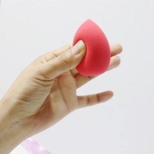 Close-up of a soft rose red teardrop makeup sponge showing its flexible texture