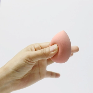 Close-up of soft peach teardrop makeup sponge being squeezed to show high elasticity