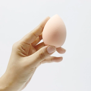 Close-up of a soft pink teardrop makeup sponge held by a hand showing fine texture