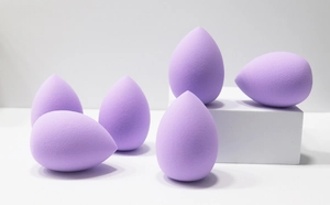 Close-up of six purple teardrop makeup sponges on white geometric display stands