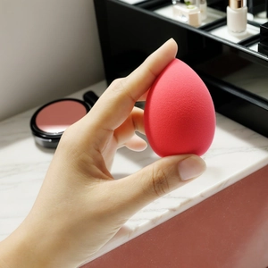 Red teardrop beauty sponge held by hand for smooth liquid foundation application