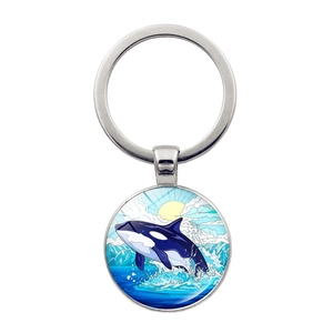 Detail of round silver keychain showing a glass orca pendant leaping over ocean mountains