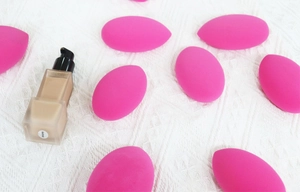 Detail of bright pink teardrop and slanted makeup sponges with foundation bottle