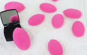 Macro detail of rose pink teardrop beauty sponges with a black mirrored makeup compact
