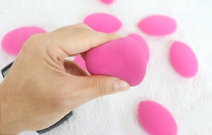Close-up of bright pink teardrop makeup sponge showing its soft texture and elasticity