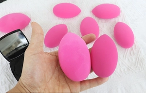 Macro shot of rose red makeup sponge held by hand against a white knit fabric background