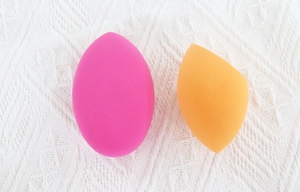 Detail view of two makeup sponges in drop and slanted shapes on a textured background