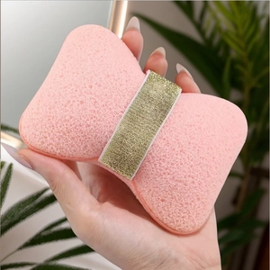 Pink bow-shaped facial sponge with gold glitter band and soft porous texture
