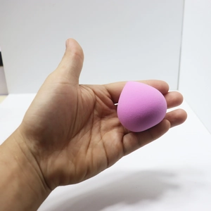 Pink teardrop beauty sponge for makeup application held in hand against white background