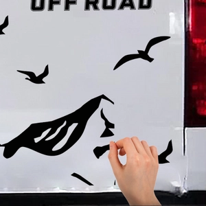 Applying black off-road decals with mountain and seagull silhouettes to a white car