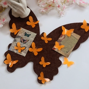 Detail of brown butterfly felt notice board with orange butterfly push pins on a white desk