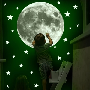 Child touching large moon and stars glow in the dark wall stickers on dark green background