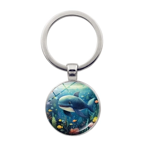 Detail of round silver keychain pendant with cartoon whale illustration on deep blue background