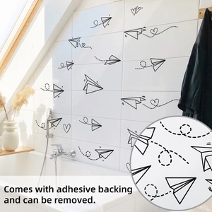 Detailed view of removable paper plane wall stickers on white bathroom tiles
