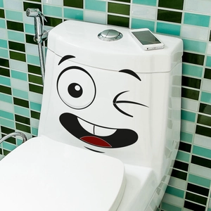 Funny winking cartoon face sticker applied on white ceramic toilet tank in bathroom