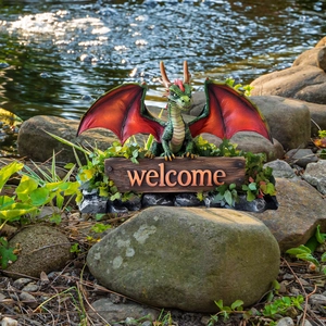 Garden dragon statue with welcome sign and red wings in outdoor landscaping setting