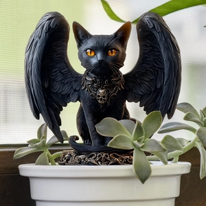 Close-up of gothic black winged cat statue with skull charm and orange eyes in garden