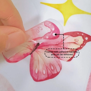 Détail montrant une main décollant un autocollant papillon rose à dos adhésif