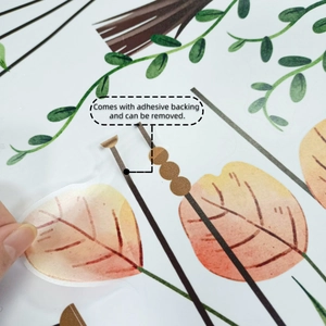 Detail showing hand peeling a self-adhesive autumn leaf wall sticker from backing paper