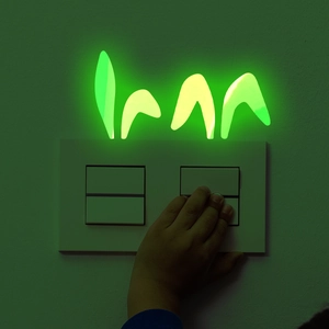 Luminous green grass wall sticker glowing in dark near light switch in kids room