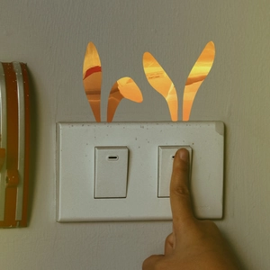 Close-up of golden mirror bunny ears switch sticker on a light wall with a hand