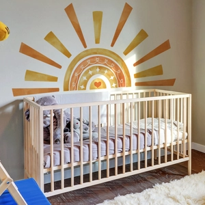 Boho sun and rainbow wall decal with hearts above a crib in a warm nursery setting