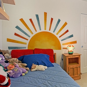 Watercolor sun wall decal with colorful rays decorating a cozy child's bedroom wall