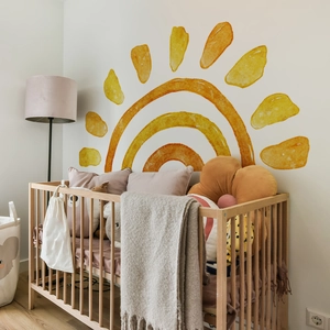 Detail of warm yellow watercolor sun wall decal in a cozy nursery room setting