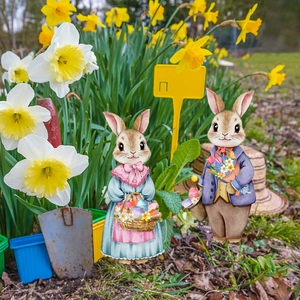 Detail of cute rabbit couple garden stakes with floral basket in a spring flower bed