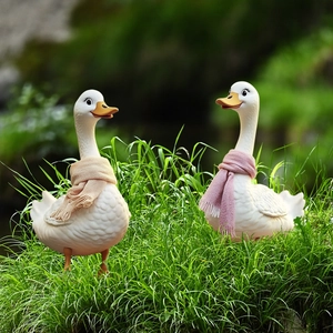 Garden duck ornaments with cozy knitted scarves in a green lawn setting for outdoor decor
