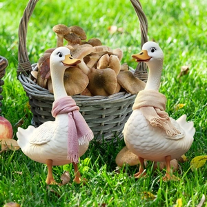 Two plastic scarf-wearing duck garden statues displayed on a lush green lawn
