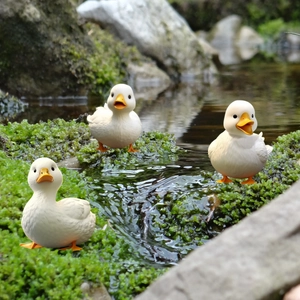Three white duck garden statues on mossy stones by a stream for outdoor landscape decor
