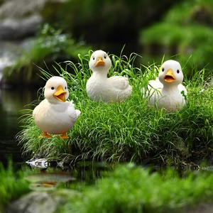 Three realistic white duck garden ornaments with orange beaks on lush green grass