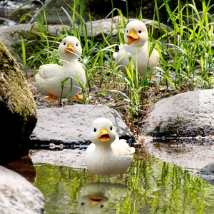 Detailed view of three white garden duck statues by a natural stream with water reflections