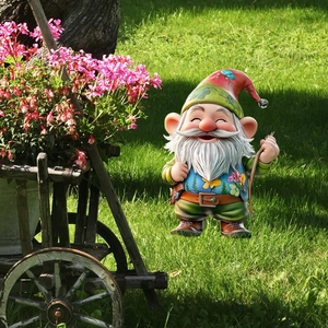 Garden gnome decoration with colorful hat on a sunny lawn next to a flower wheelbarrow